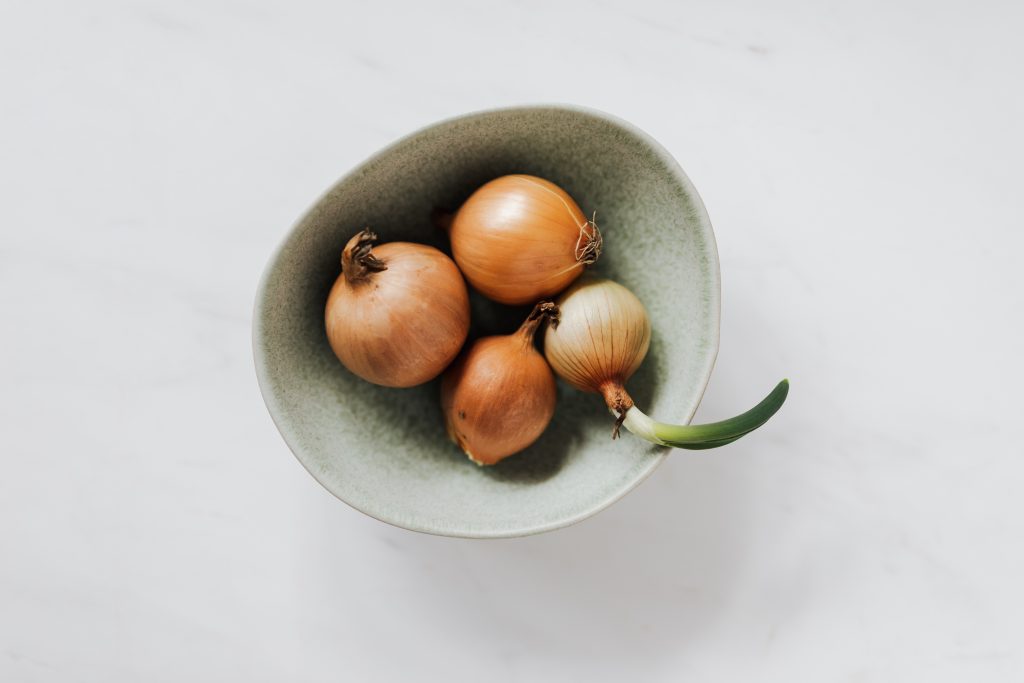 Bowl with raw onion bulbs on marble surface